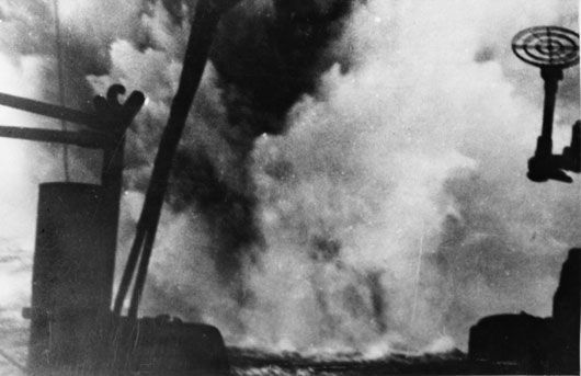 Water sprays into the air from a near miss during an attack on HMAS Perth by German bomber aircraft during the evacuation of Australian soldiers from Greece (AWM 306799).